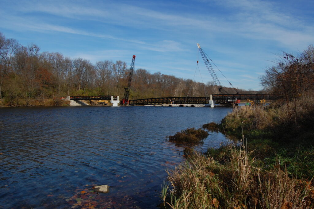 A low railroad bridge over a river in Midwestern America. Cranes are raising the middle section to join the two end pieces. 